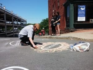 A street artist decorates one of the Enjoy Troy decals in the crosswalk at the intersection of State and River Streets in downtown Troy during River Fest on Saturday, June 18.